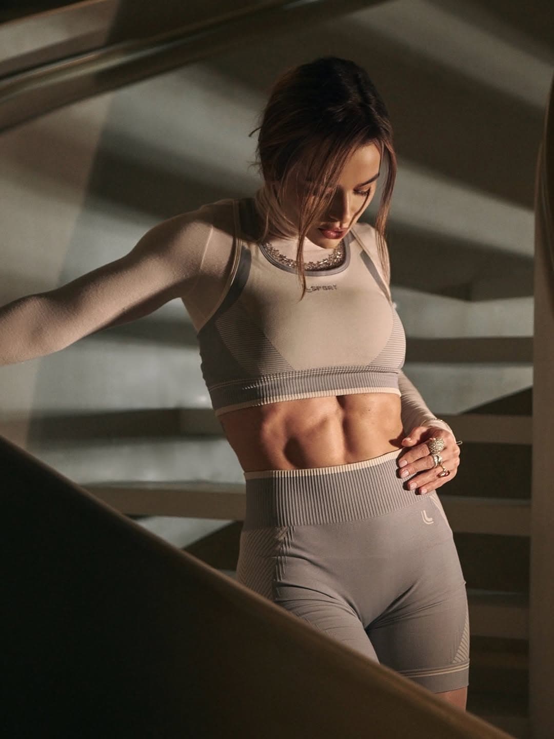 A fitness training business showcases an athlete in coordinated workout wear, standing on a staircase and looking down at her midsection.